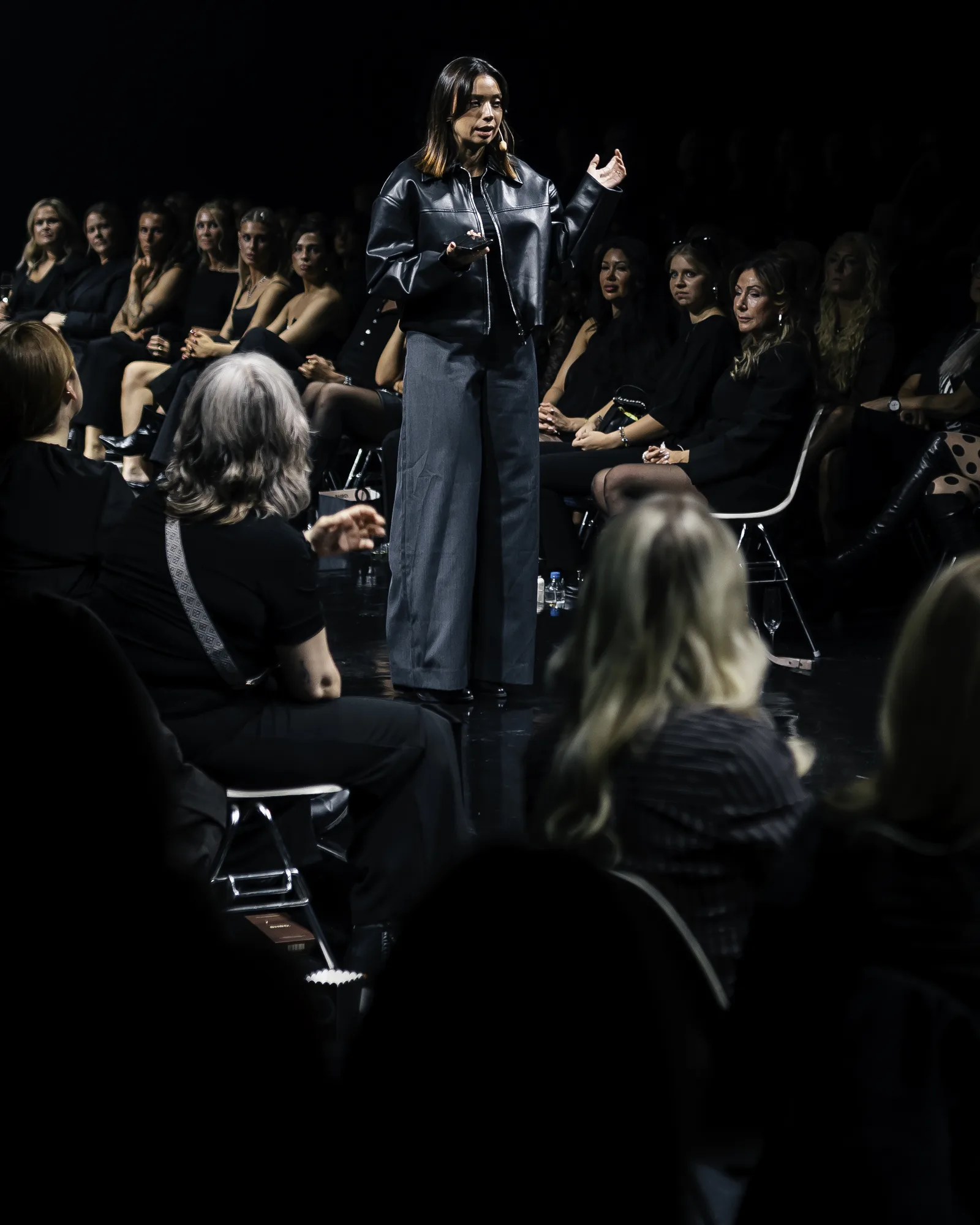 Nicole Boman speaking on a runway stage, surrounded by an audience