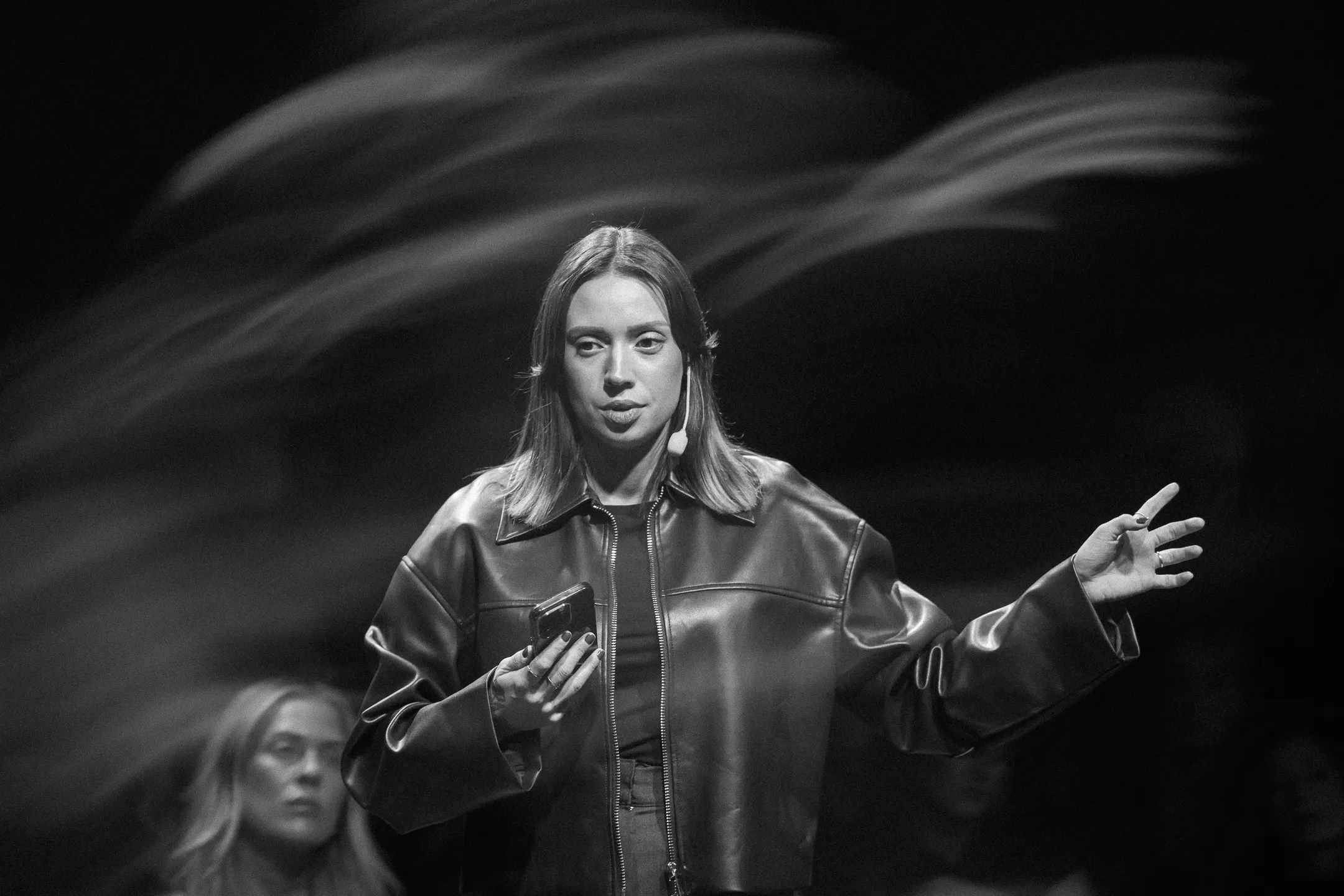 Nicole Boman on stage in a leather jacket, gesturing to the audience, black and white